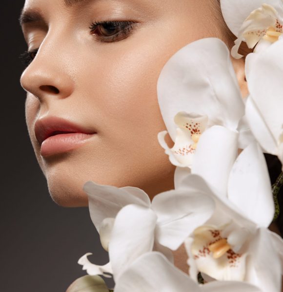 Portrait of beautiful young woman with nude make up posing with orchid flowers isolated over dark background